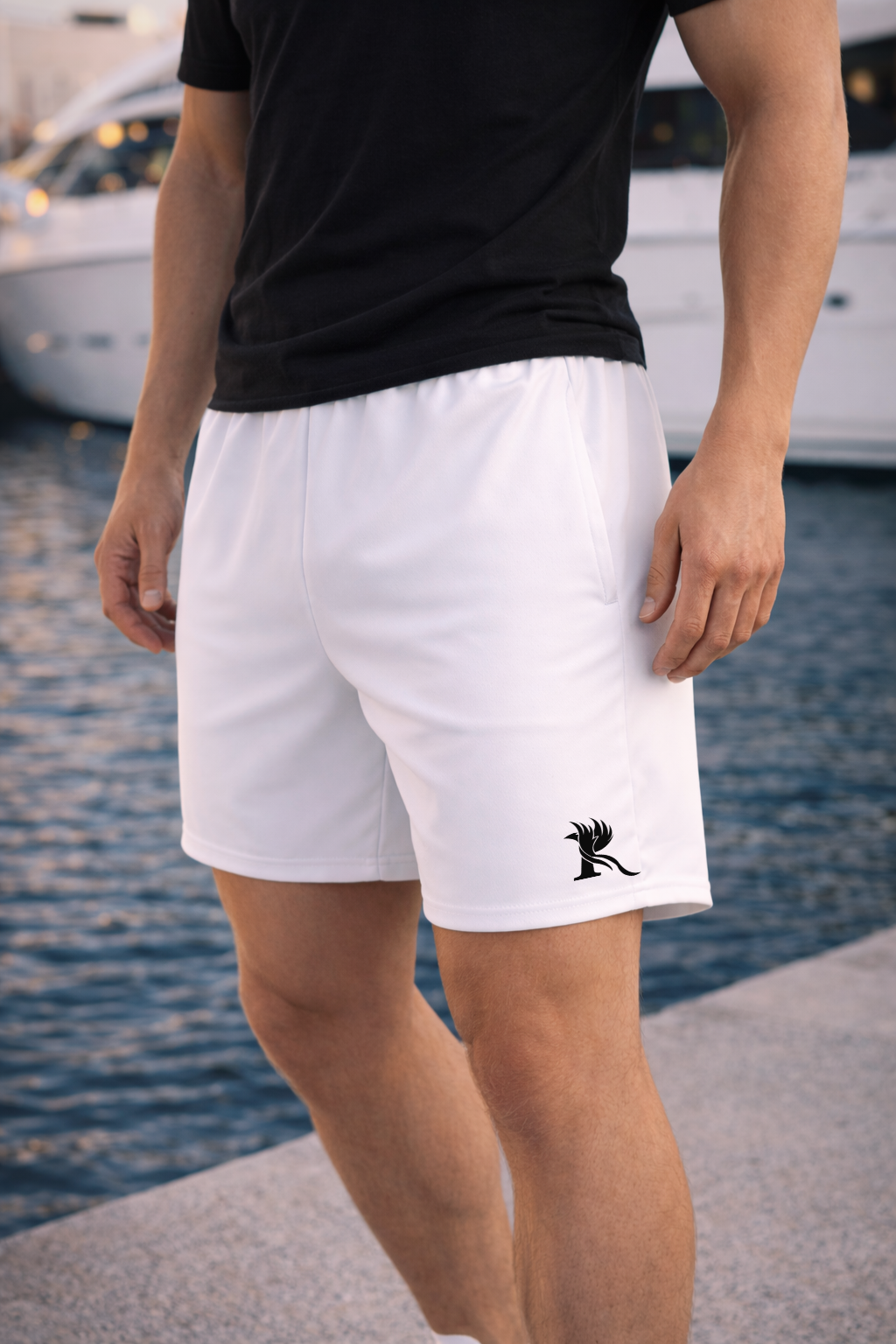Male model wearing white SOAR performance athletic shorts with black phoenix emblem near marina waterfront.