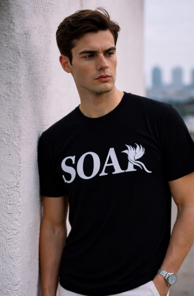 Men’s black SOAR logo t-shirt with white phoenix graphic, model leaning against wall in modern city setting, luxury streetwear style.